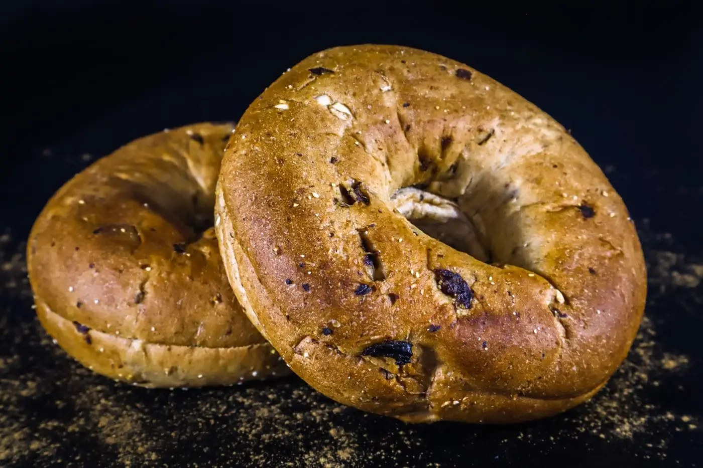 Two raisin bagels on a dark background with scattered seasoning