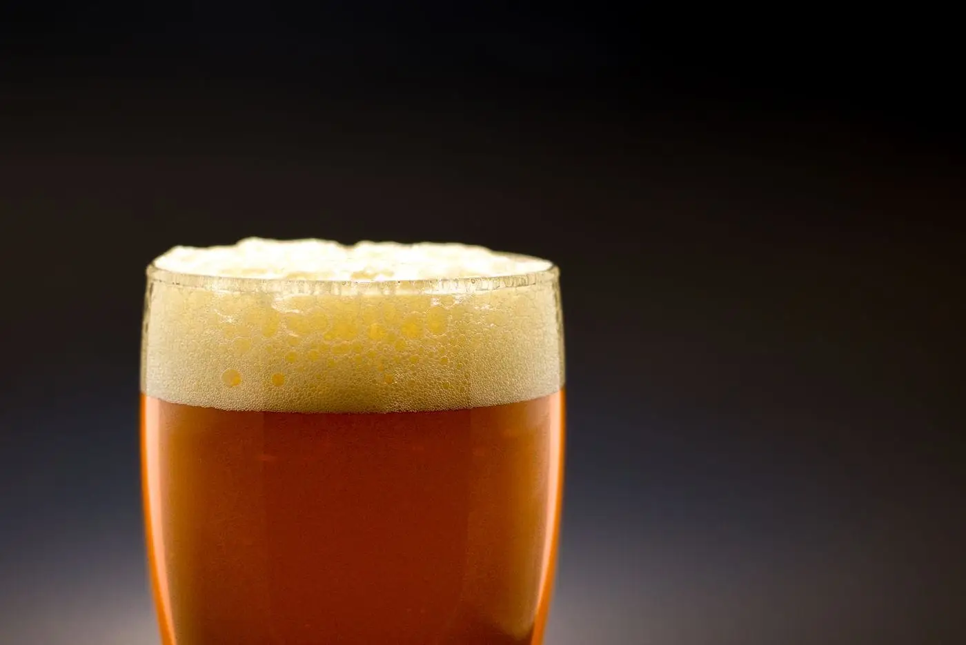 Glass of amber beer with a foamy head against a dark background