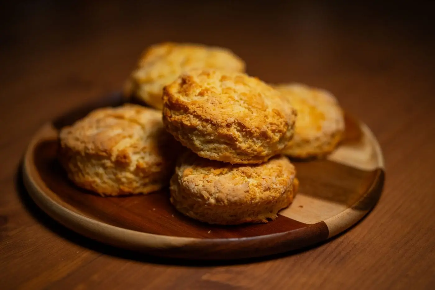 Freshly baked golden buttermilk biscuits stacked on a round wooden plate