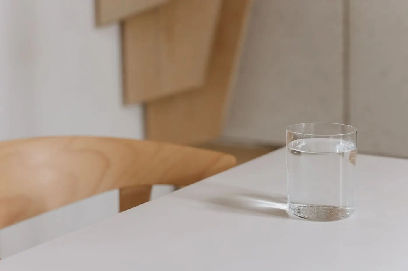 Glass of still water on a white table beside a wooden chair