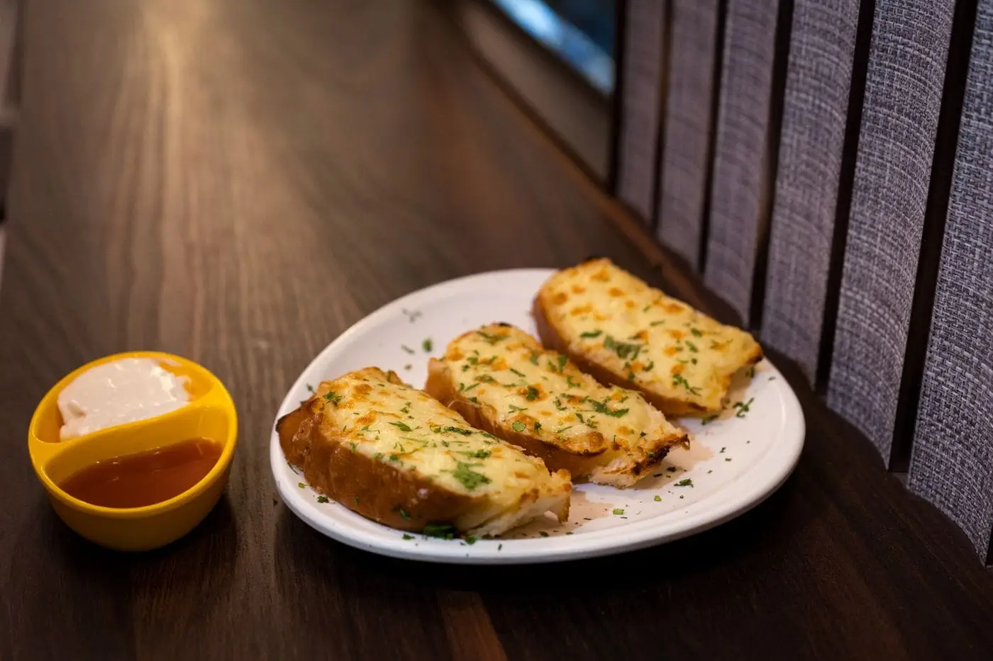 Cheesy garlic bread slices on a white plate with dipping sauces