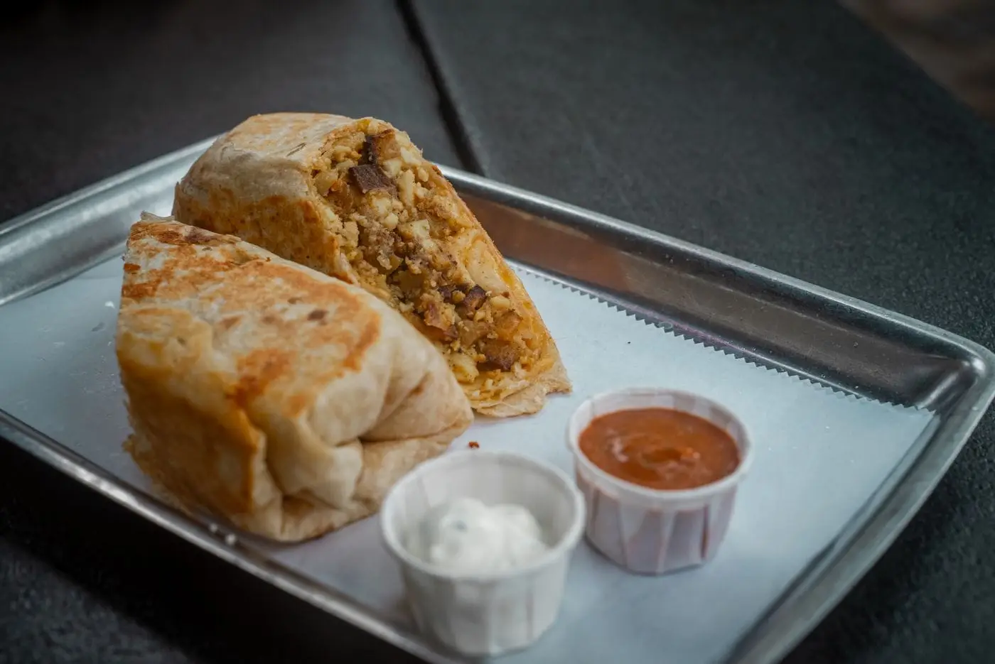 Breakfast burrito cut in half with egg filling, salsa and sour cream