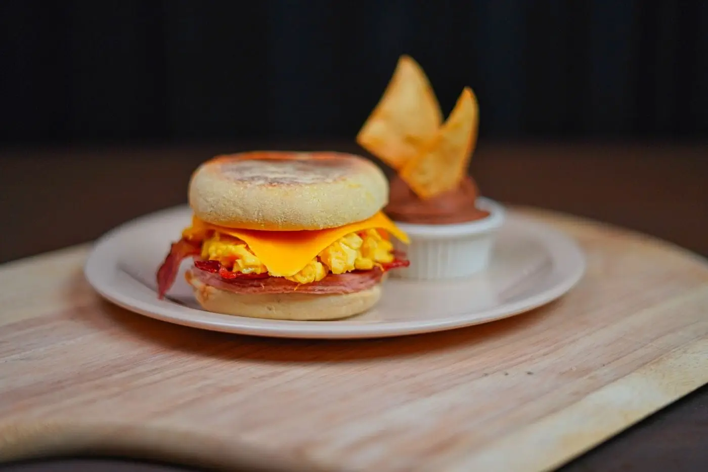 English muffin breakfast sandwich with scrambled egg, cheese and bacon on a plate