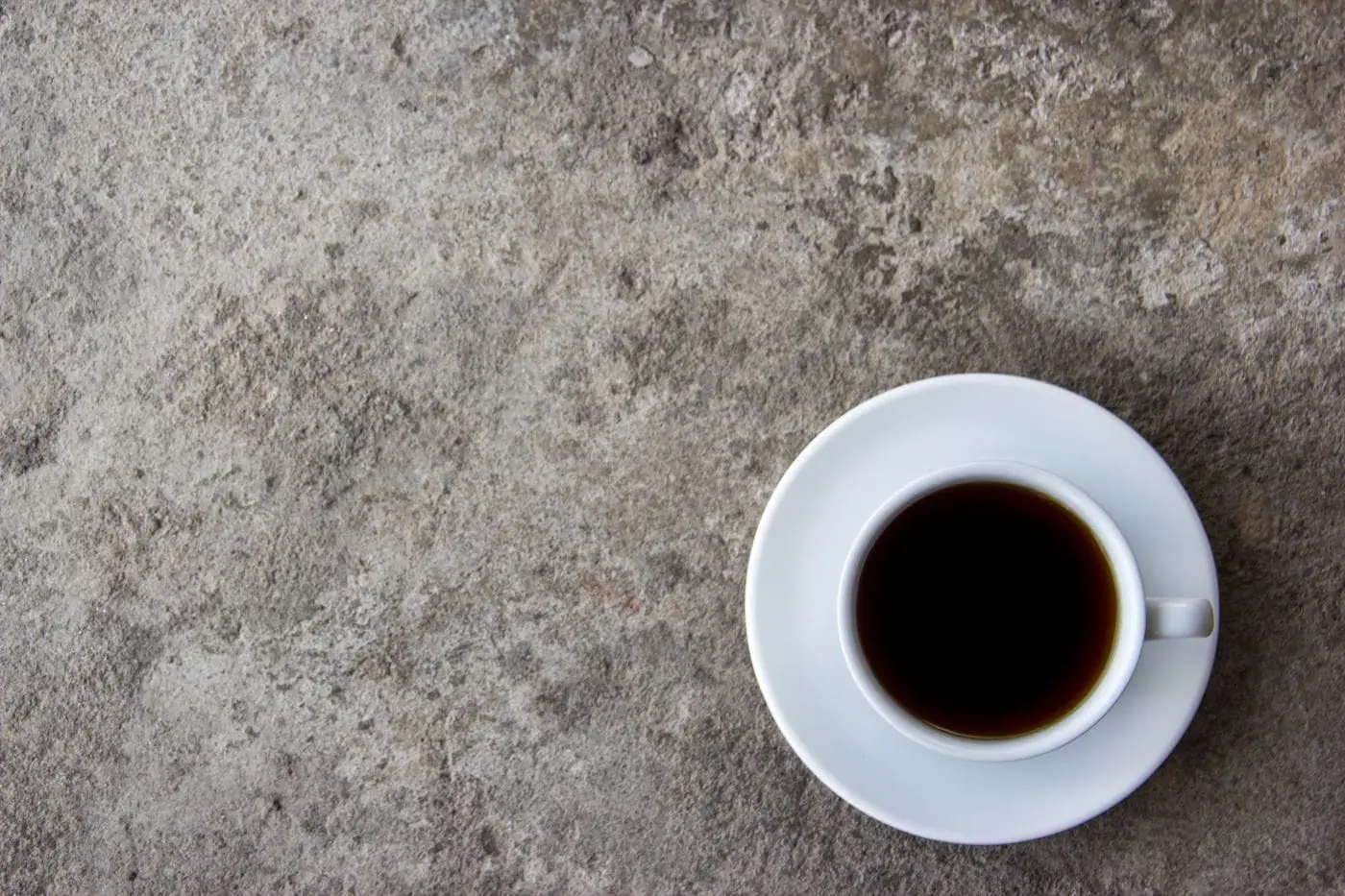 Black coffee in a white cup and saucer on a gray stone surface
