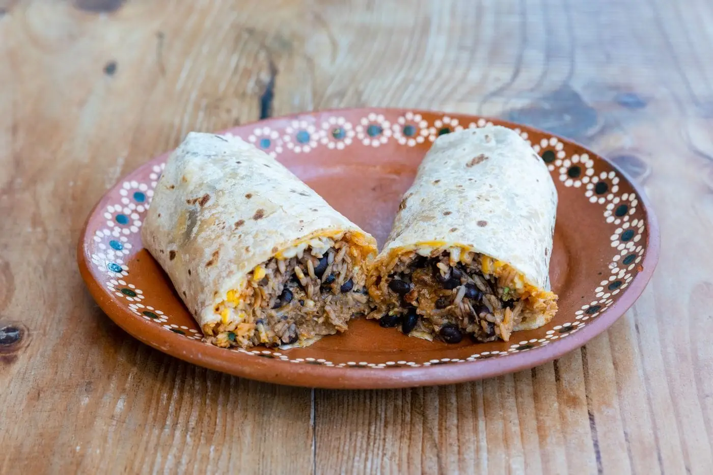 Burrito cut in half showing rice, beans and meat on a clay plate