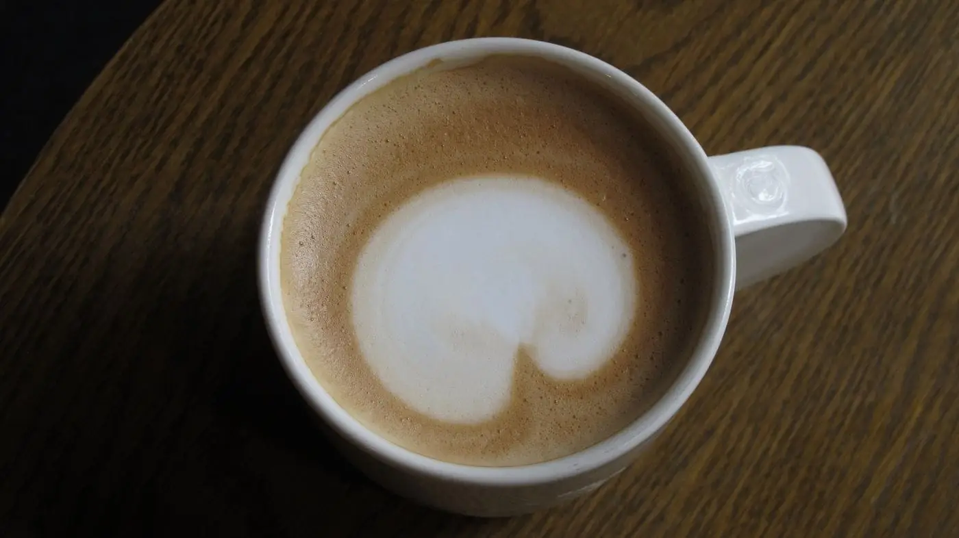 Top view of a frothy cappuccino in a white cup on a wooden table