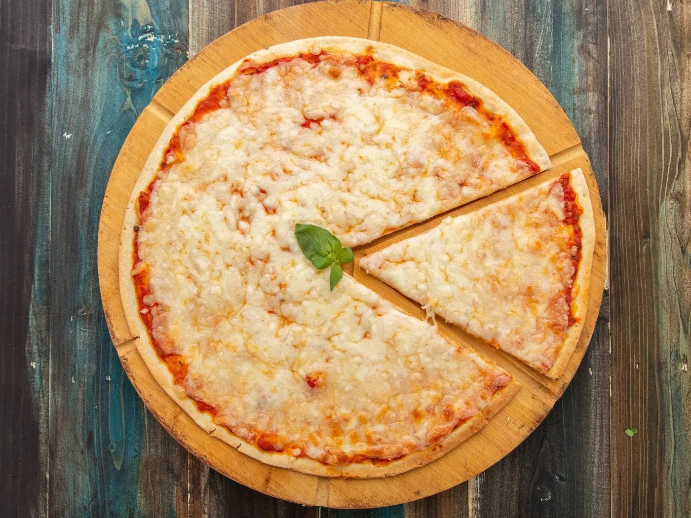 Top view of a sliced cheese pizza on a wooden board