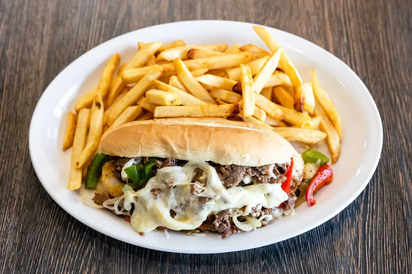 Philly cheesesteak with melted cheese and peppers on a roll with fries