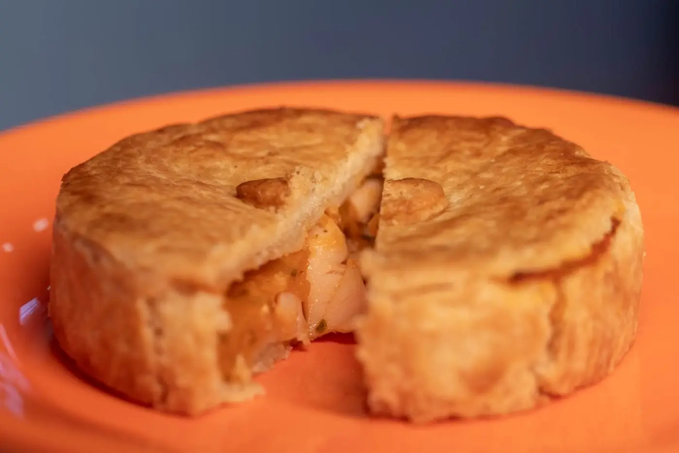 Individual chicken pot pie broken open to show filling on an orange plate