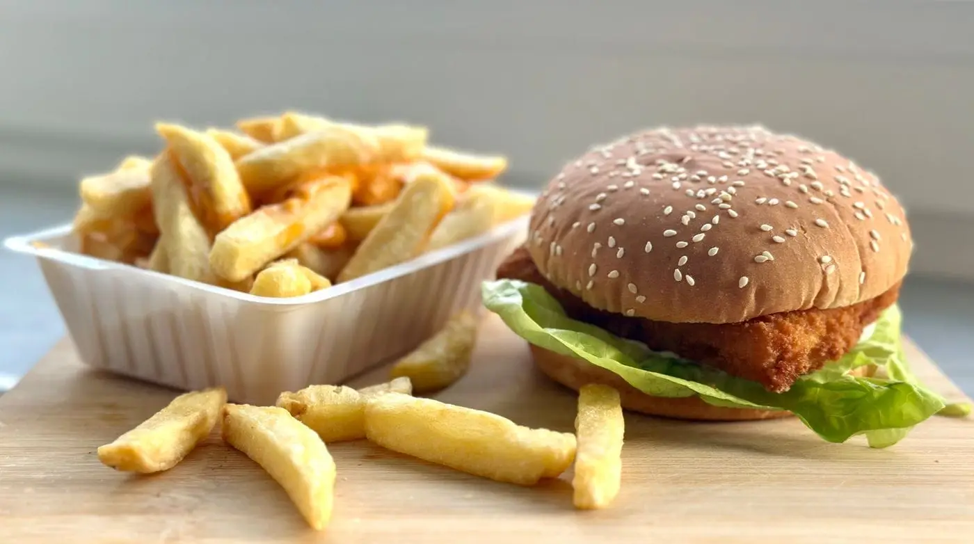 Crispy fried chicken sandwich with lettuce on a sesame bun beside fries