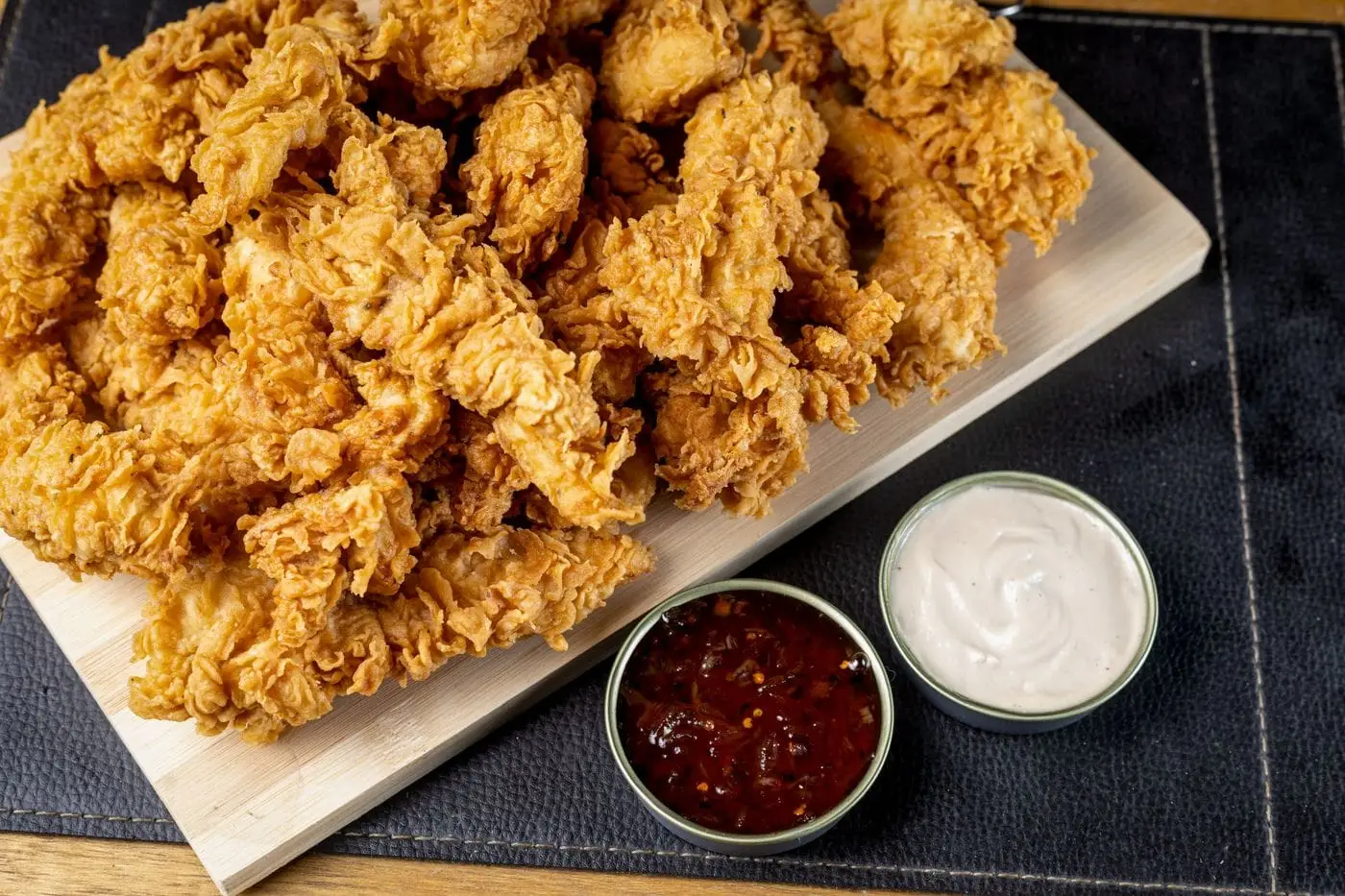 Crispy fried chicken tenders on a board with two dipping sauces