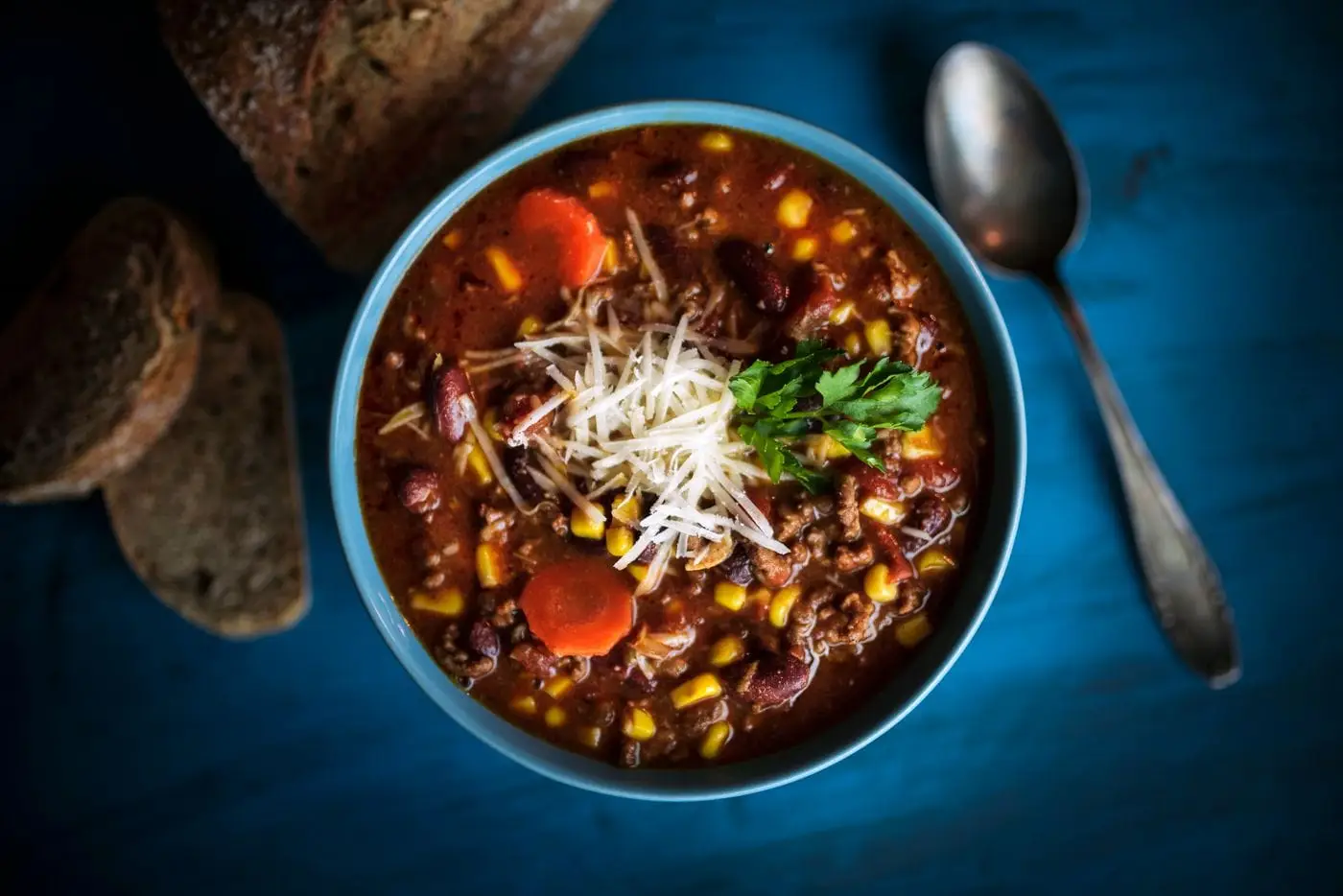 Bowl of beef chili with beans and corn topped with cheese