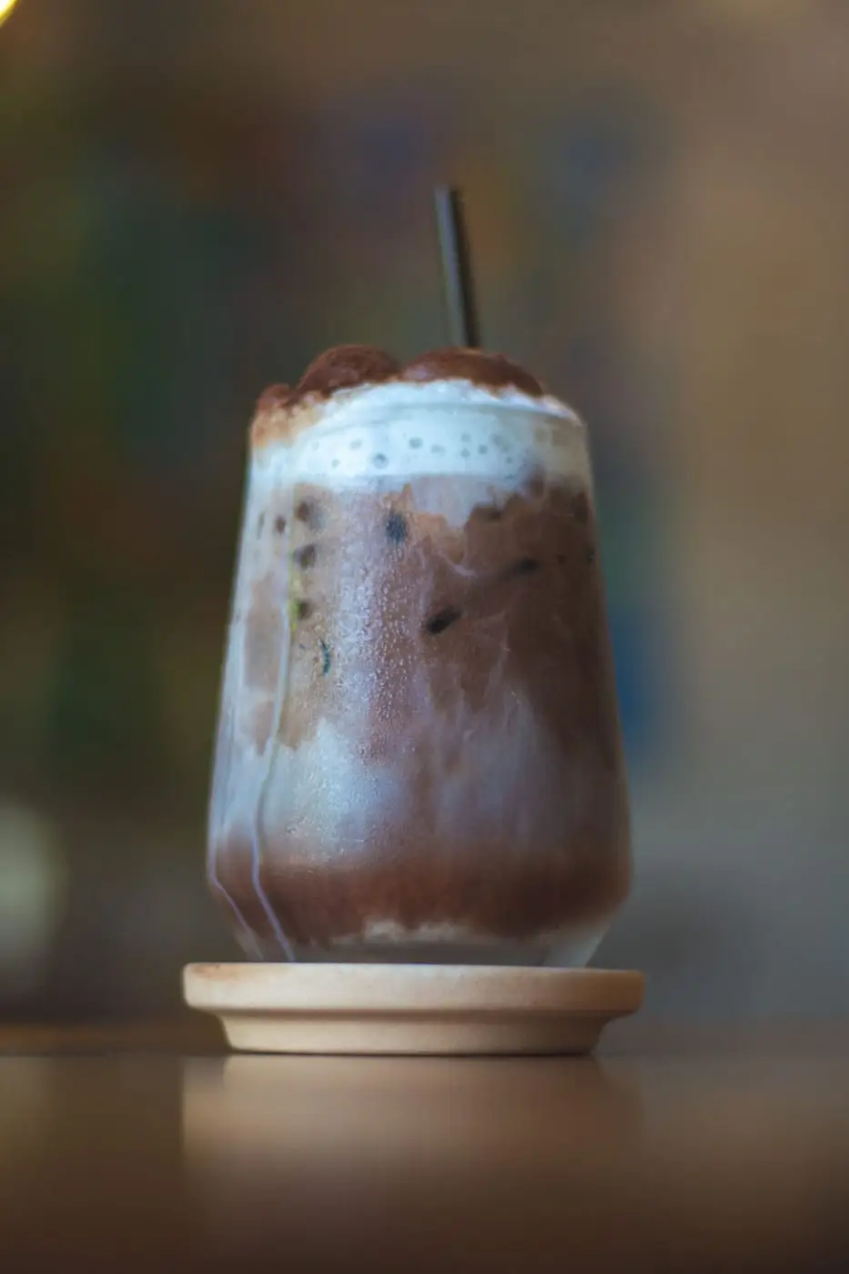 Iced chocolate milk drink with creamy froth in a glass on a coaster