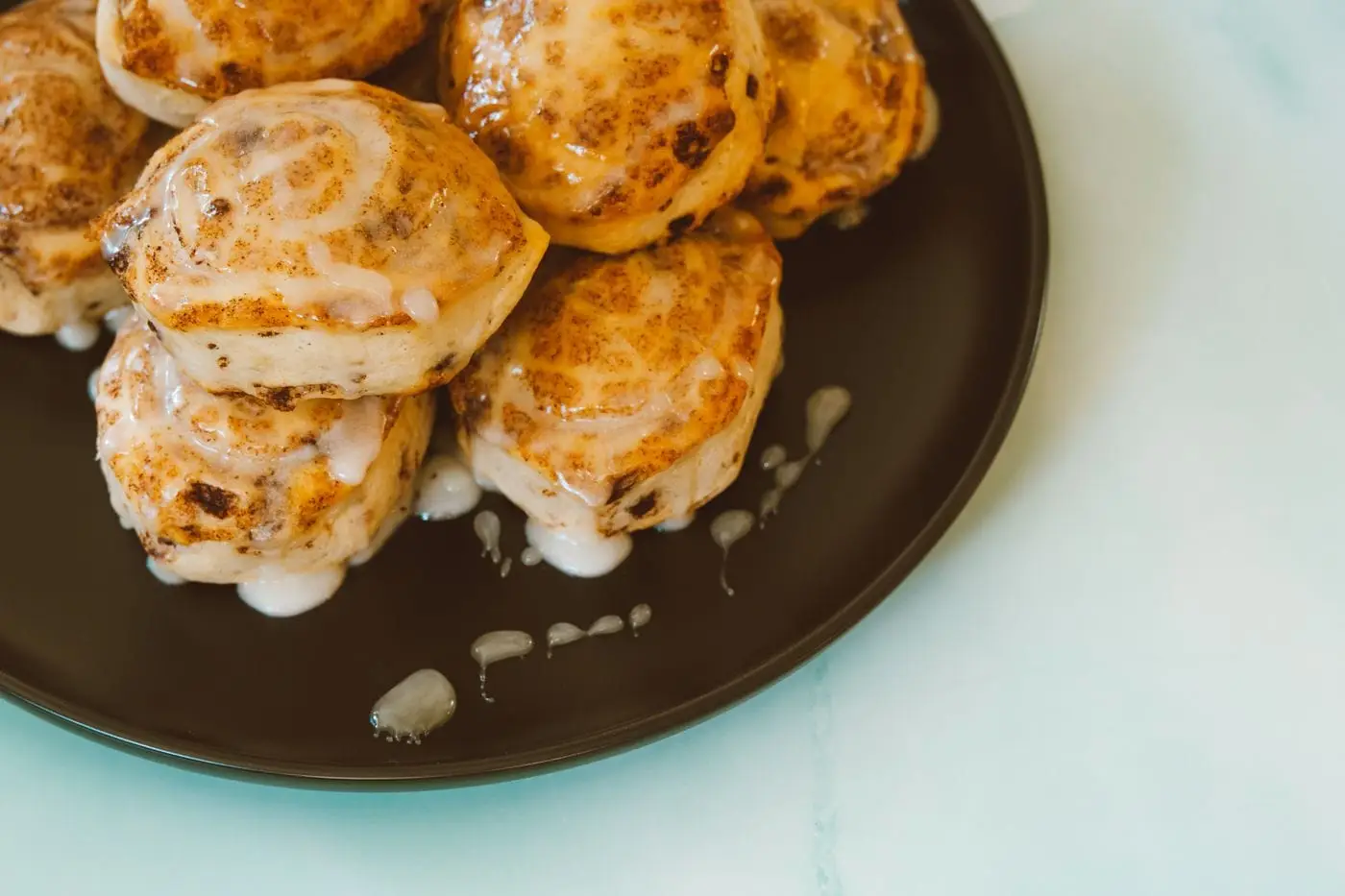 Iced cinnamon rolls piled on a dark plate with dripping glaze