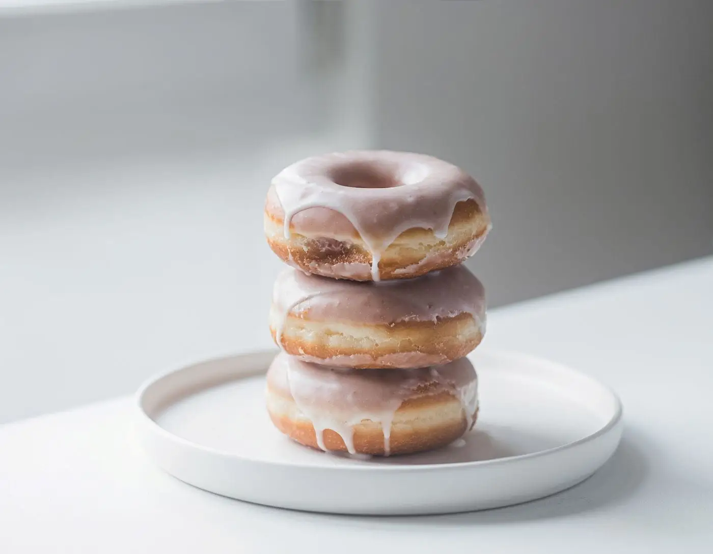 Stack of three glazed donuts on a white plate