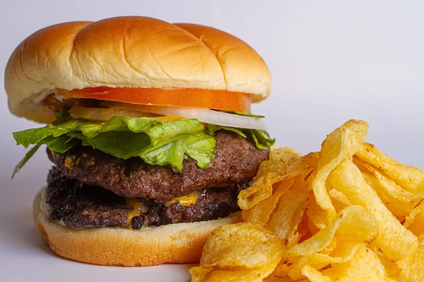 Double cheeseburger with lettuce, tomato and onion beside potato chips