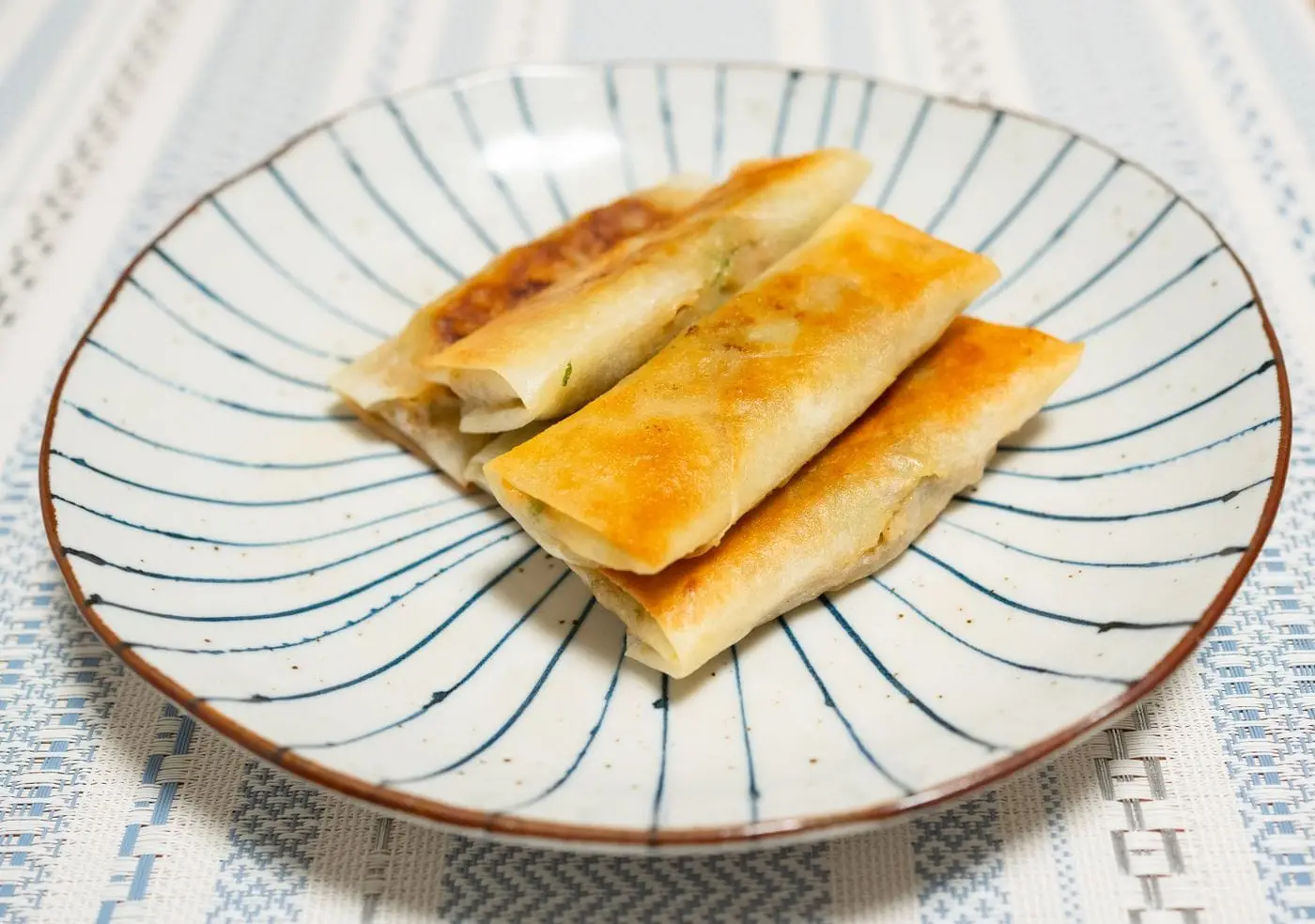 Crispy golden spring rolls on a blue-striped plate