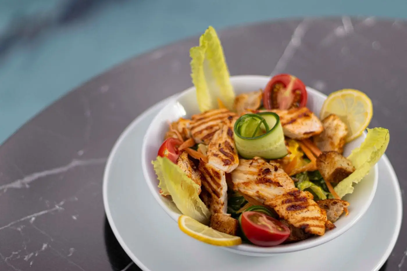 Grilled chicken salad with romaine, tomatoes, croutons and lemon in a bowl