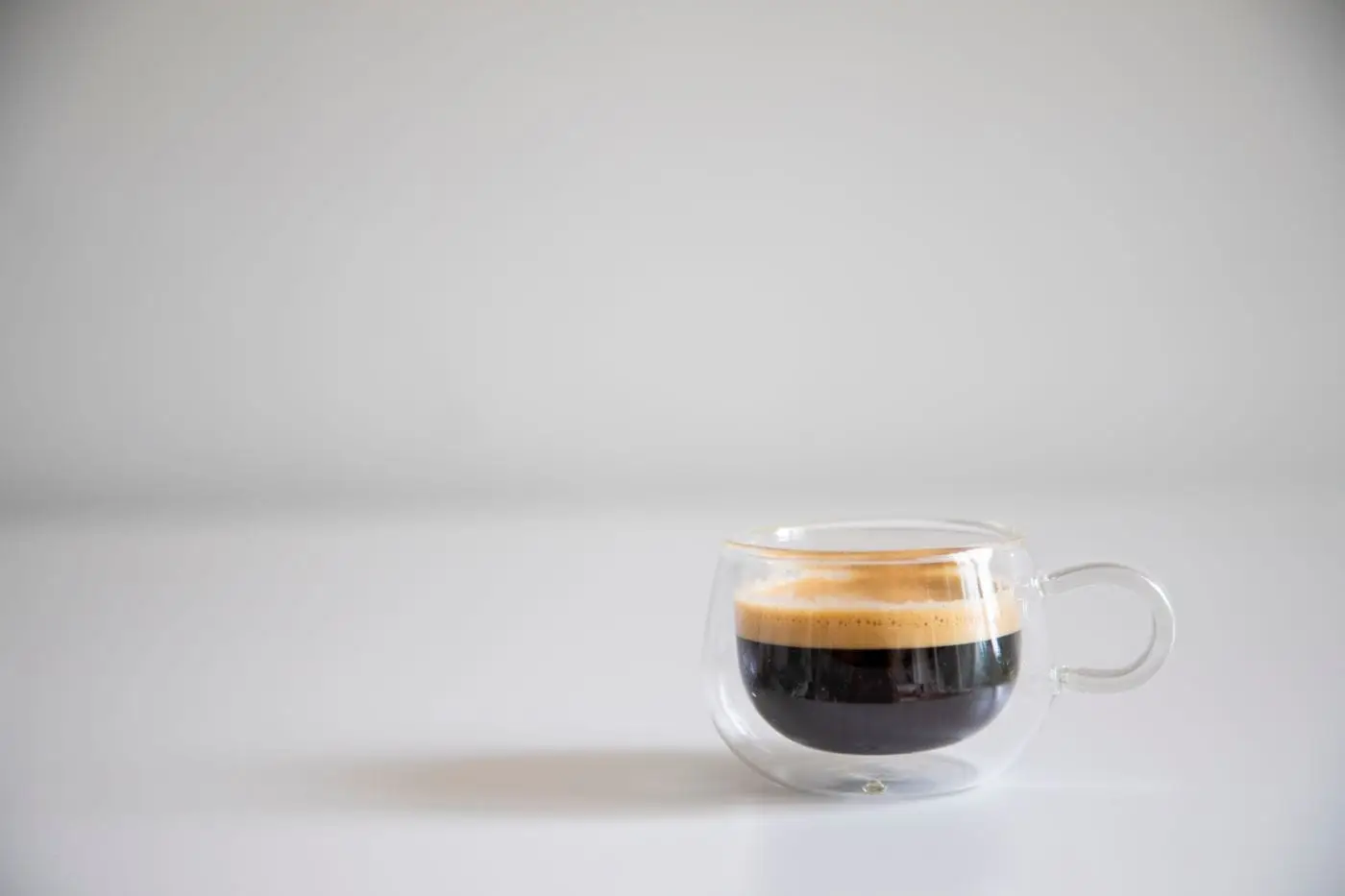Espresso shot with golden crema in a clear glass cup on white