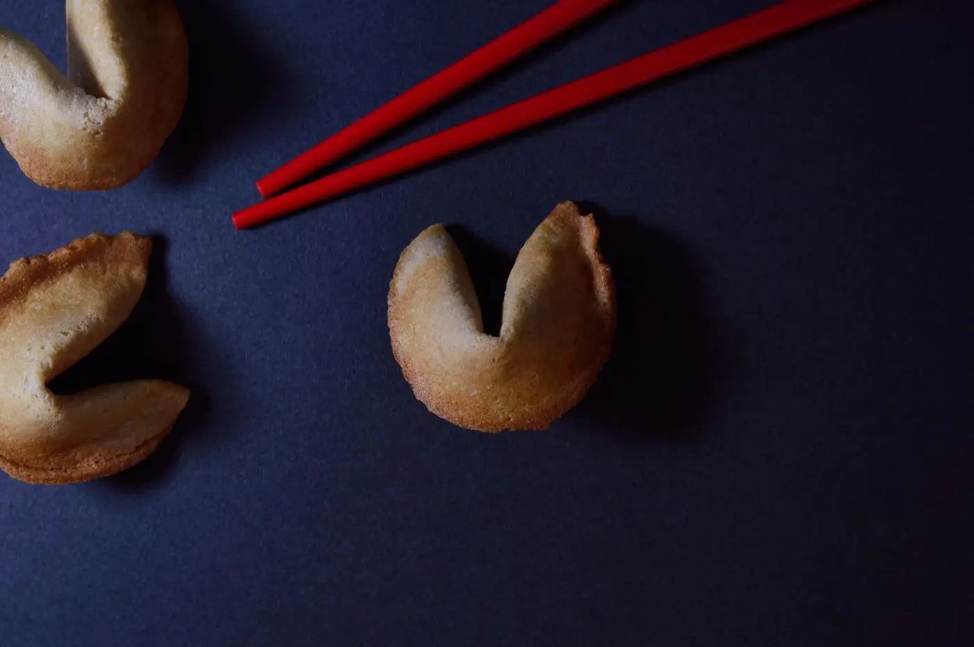 Three fortune cookies beside red chopsticks on a dark surface