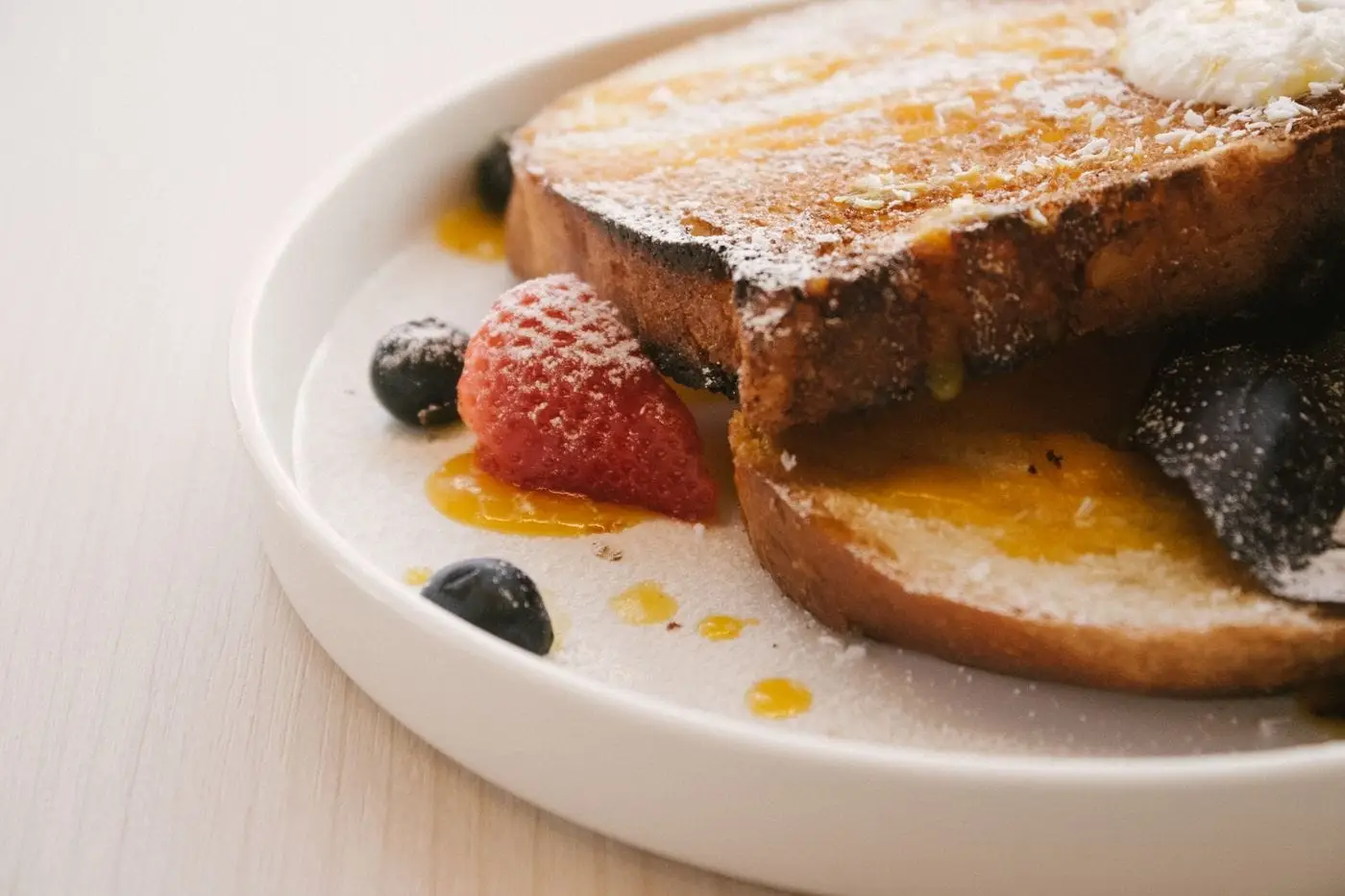 French toast with powdered sugar, syrup and berries on a white plate