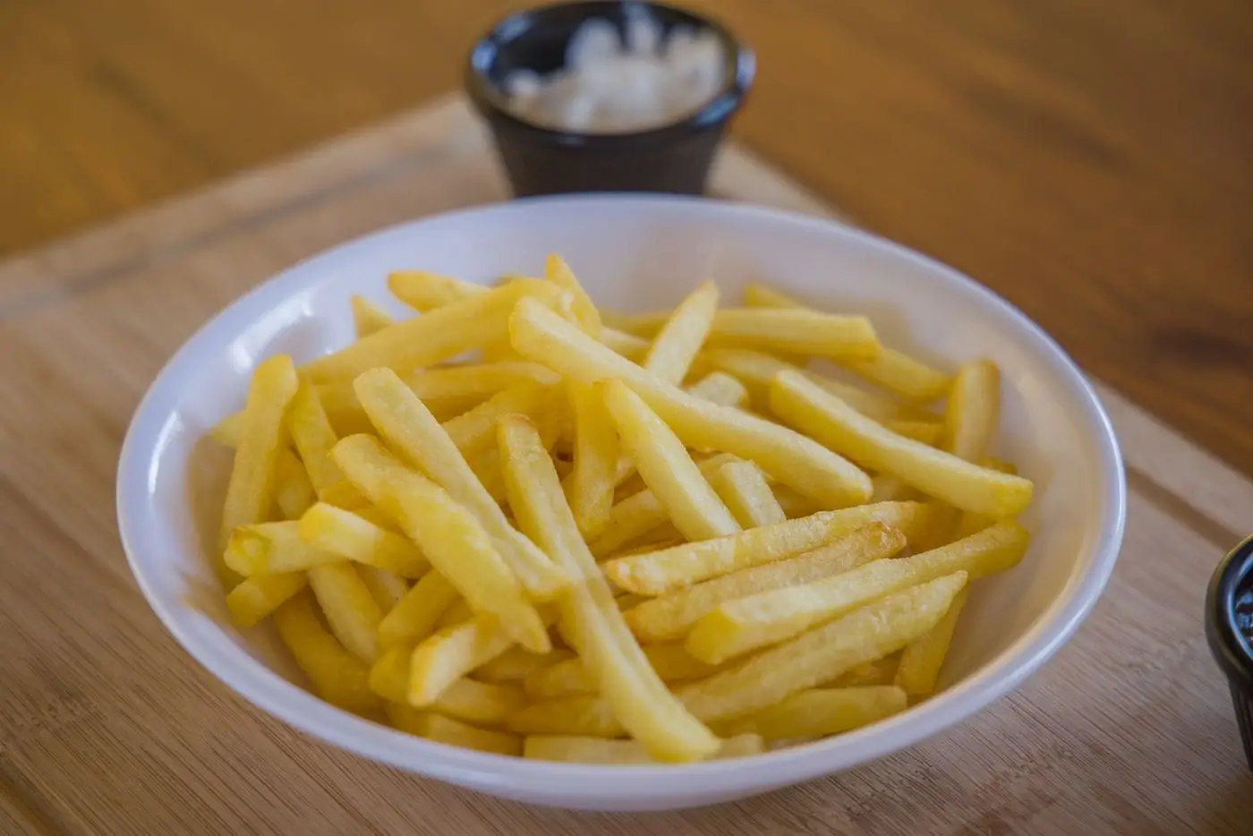 Bowl of golden french fries on a wooden board