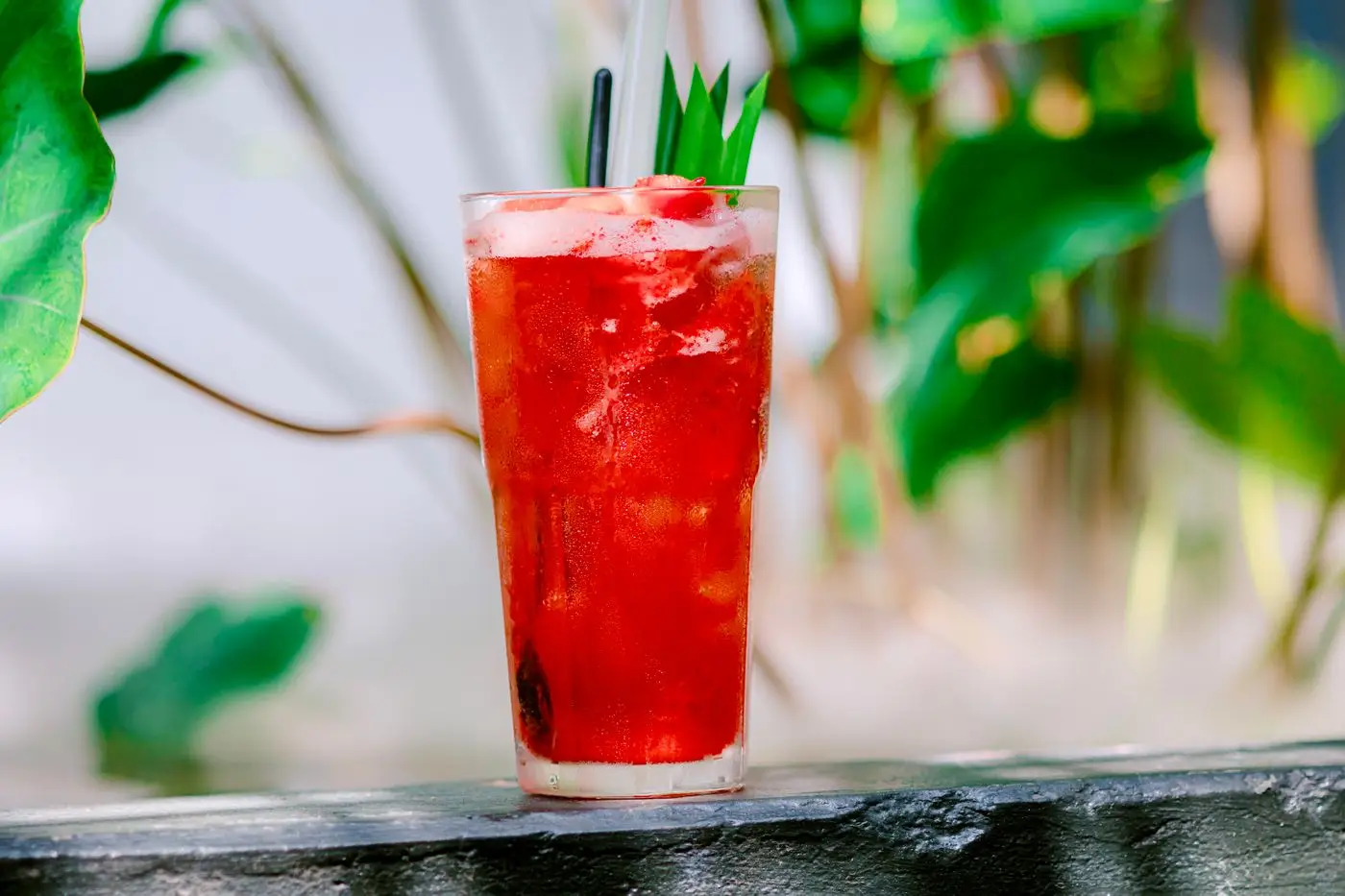 Tall glass of red fruit drink with ice and straws outdoors