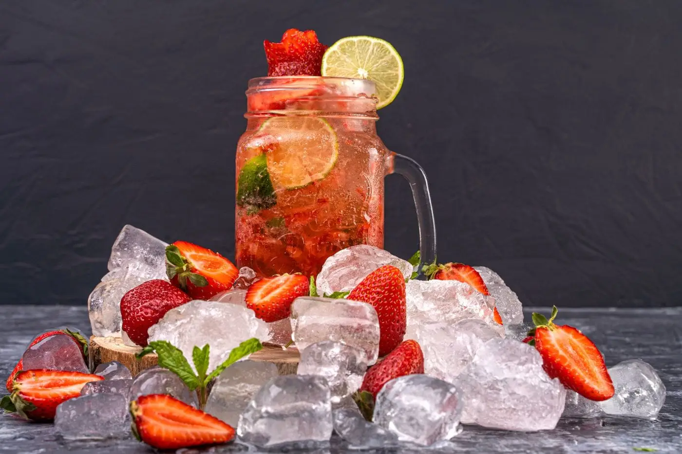Iced strawberry lime drink in a mason jar surrounded by strawberries and ice