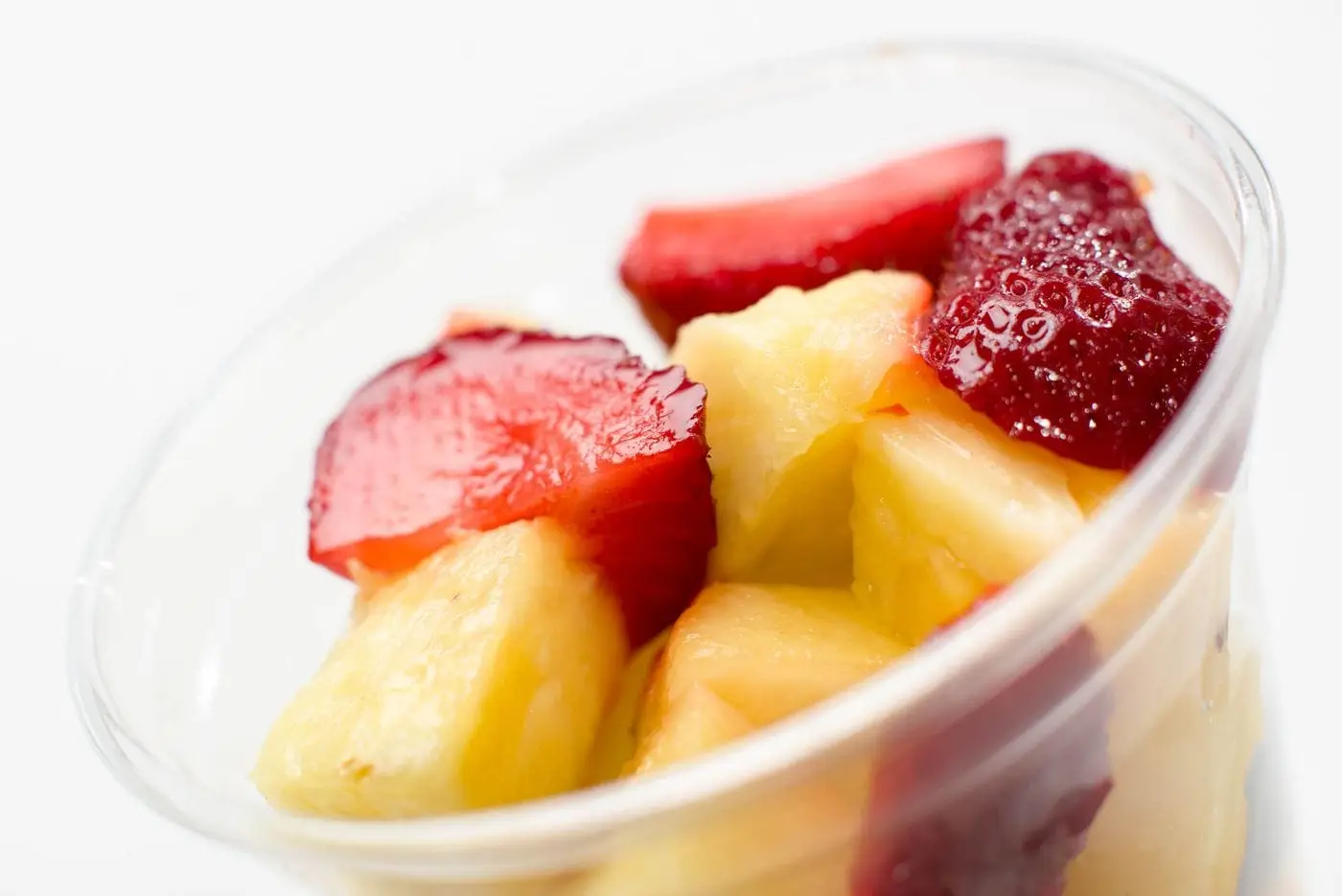Clear cup of fresh pineapple chunks and sliced strawberries