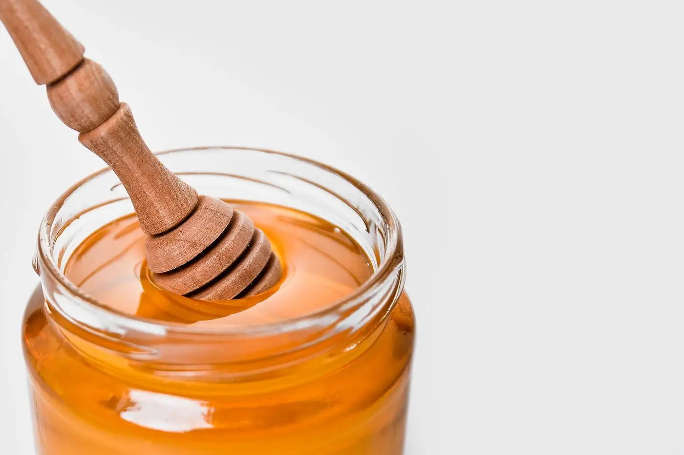 Open glass jar of golden honey with a wooden honey dipper