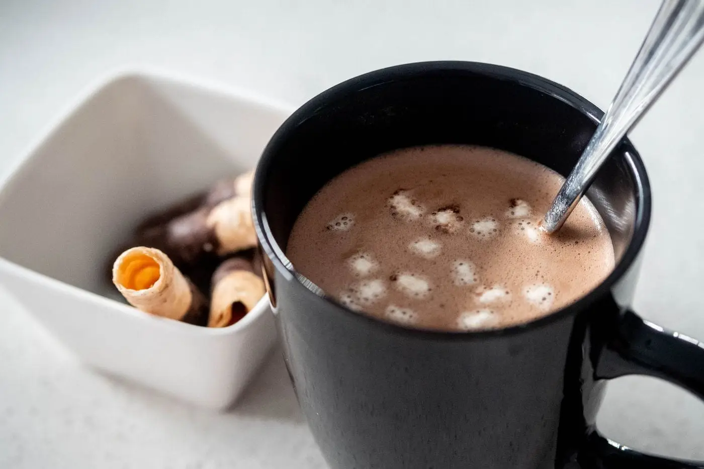 Hot chocolate with mini marshmallows in a black mug with a spoon