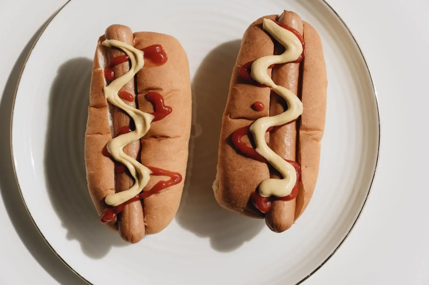 Two hot dogs in buns topped with ketchup and mustard on a plate