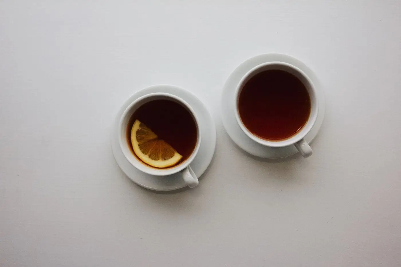Two cups of hot black tea on saucers, one with a lemon slice
