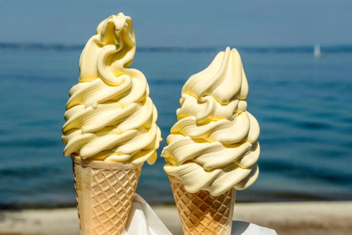 Two vanilla soft serve ice cream cones in front of the sea