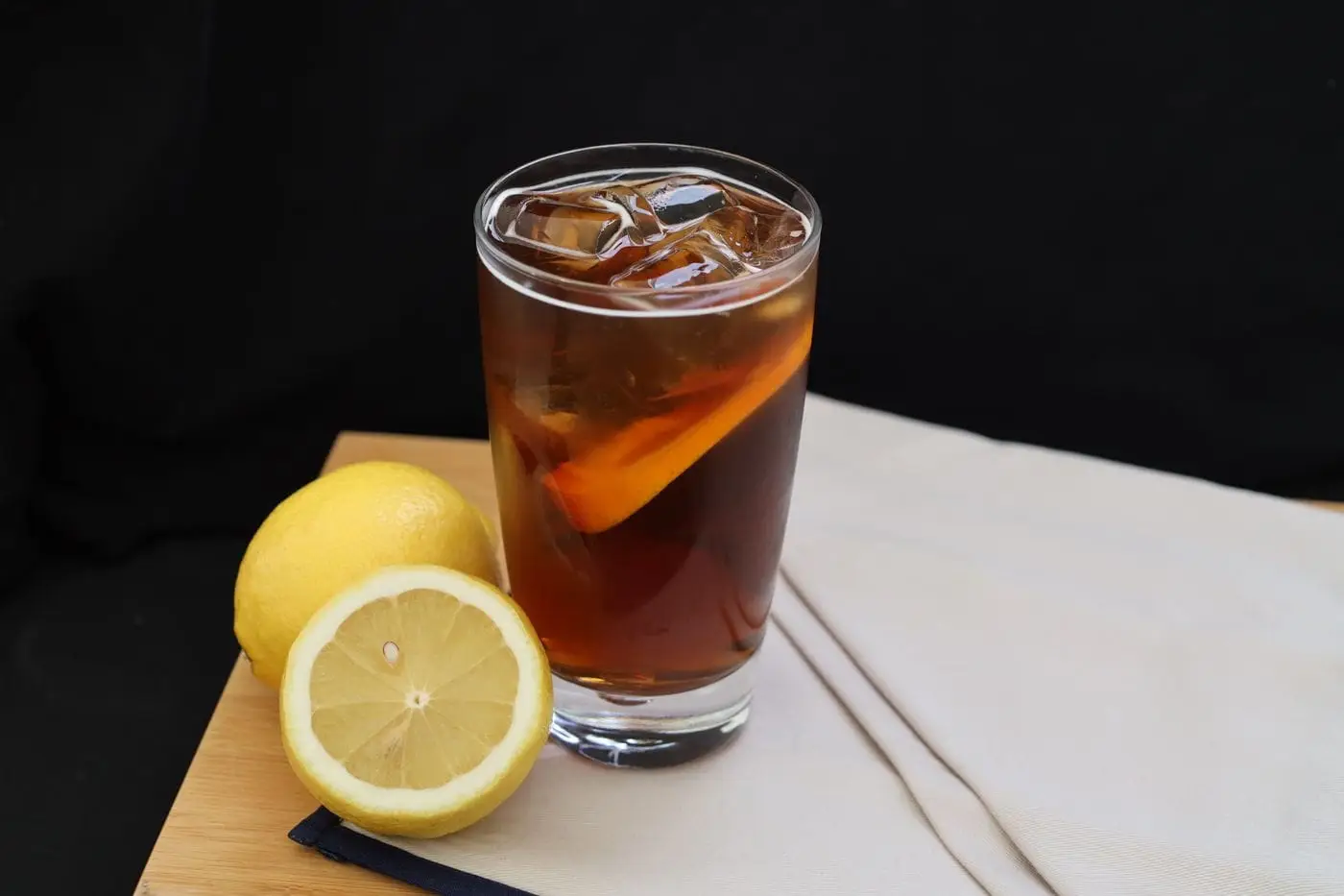 Glass of iced tea with ice cubes and a lemon slice beside lemons