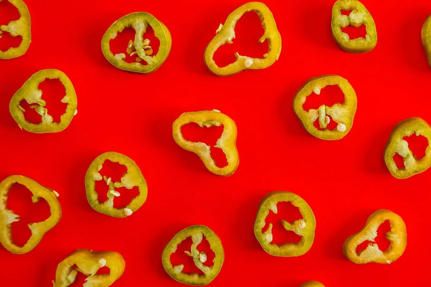 Fresh sliced jalapeño pepper rings scattered on a red background