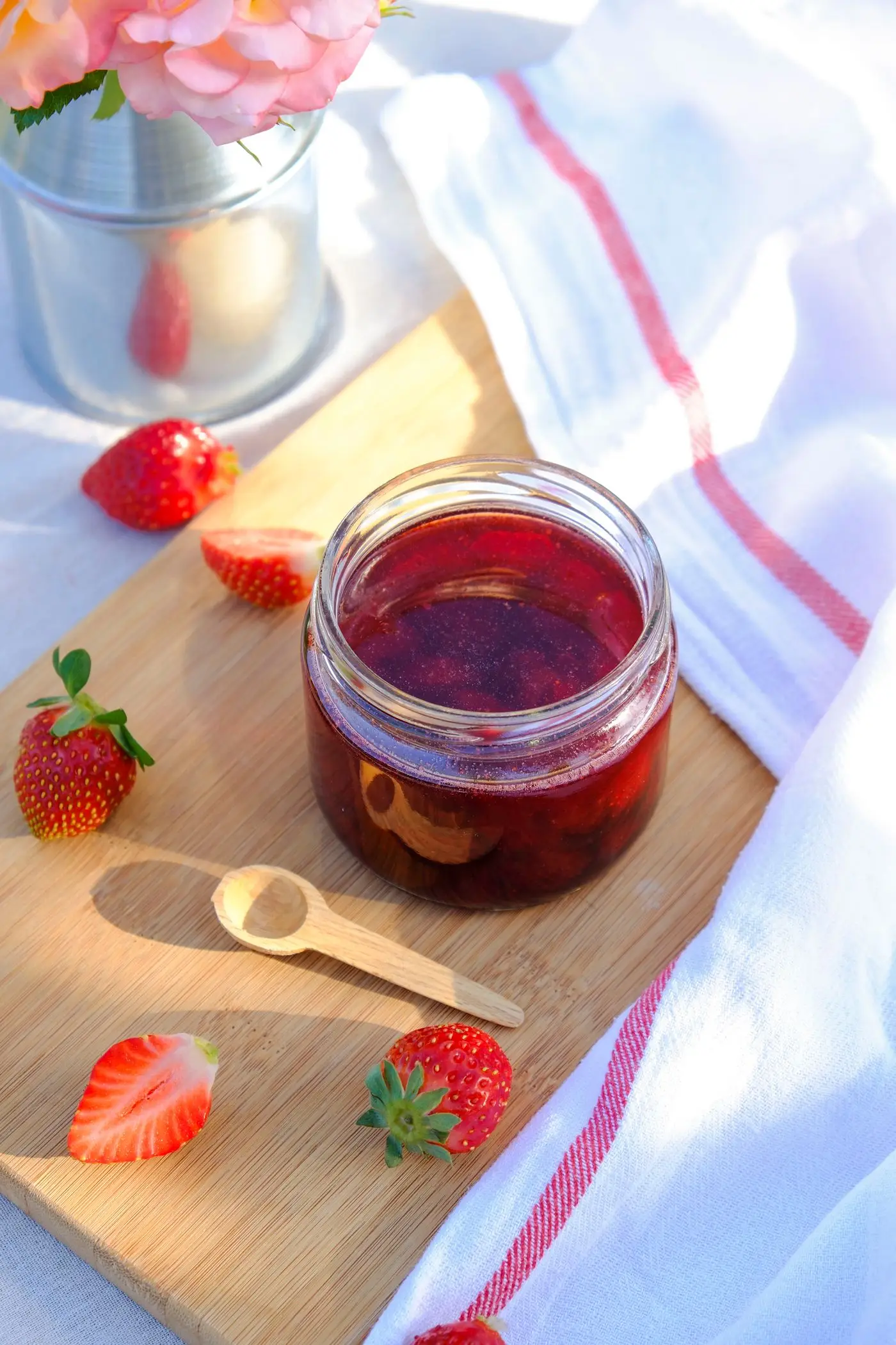Open glass jar of strawberry jam with fresh strawberries and a wooden spoon