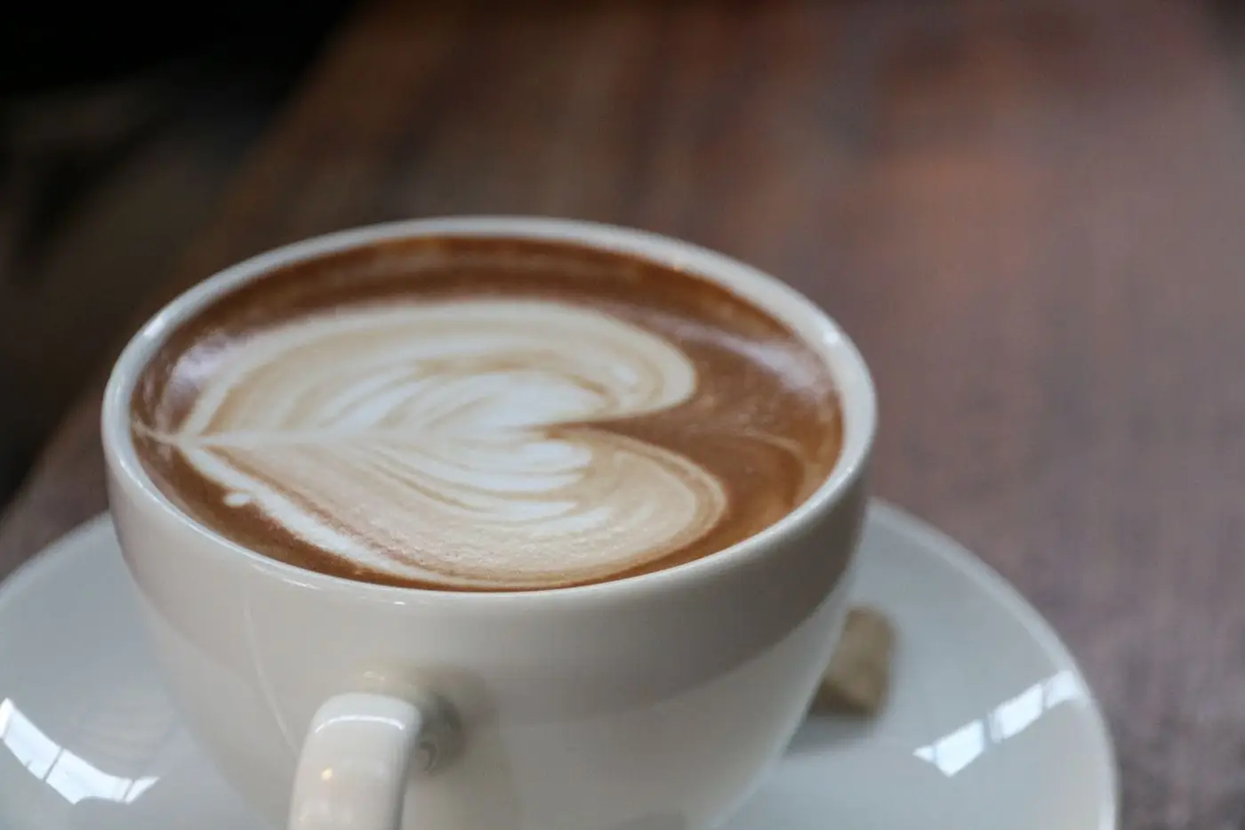 Hot latte with heart-shaped latte art in a white cup and saucer