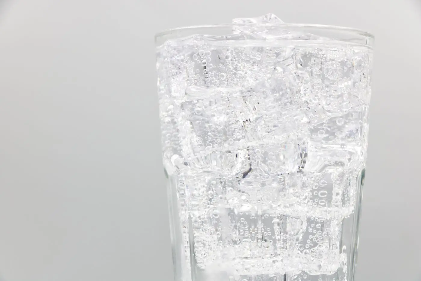 Glass of clear sparkling soda with ice cubes and bubbles
