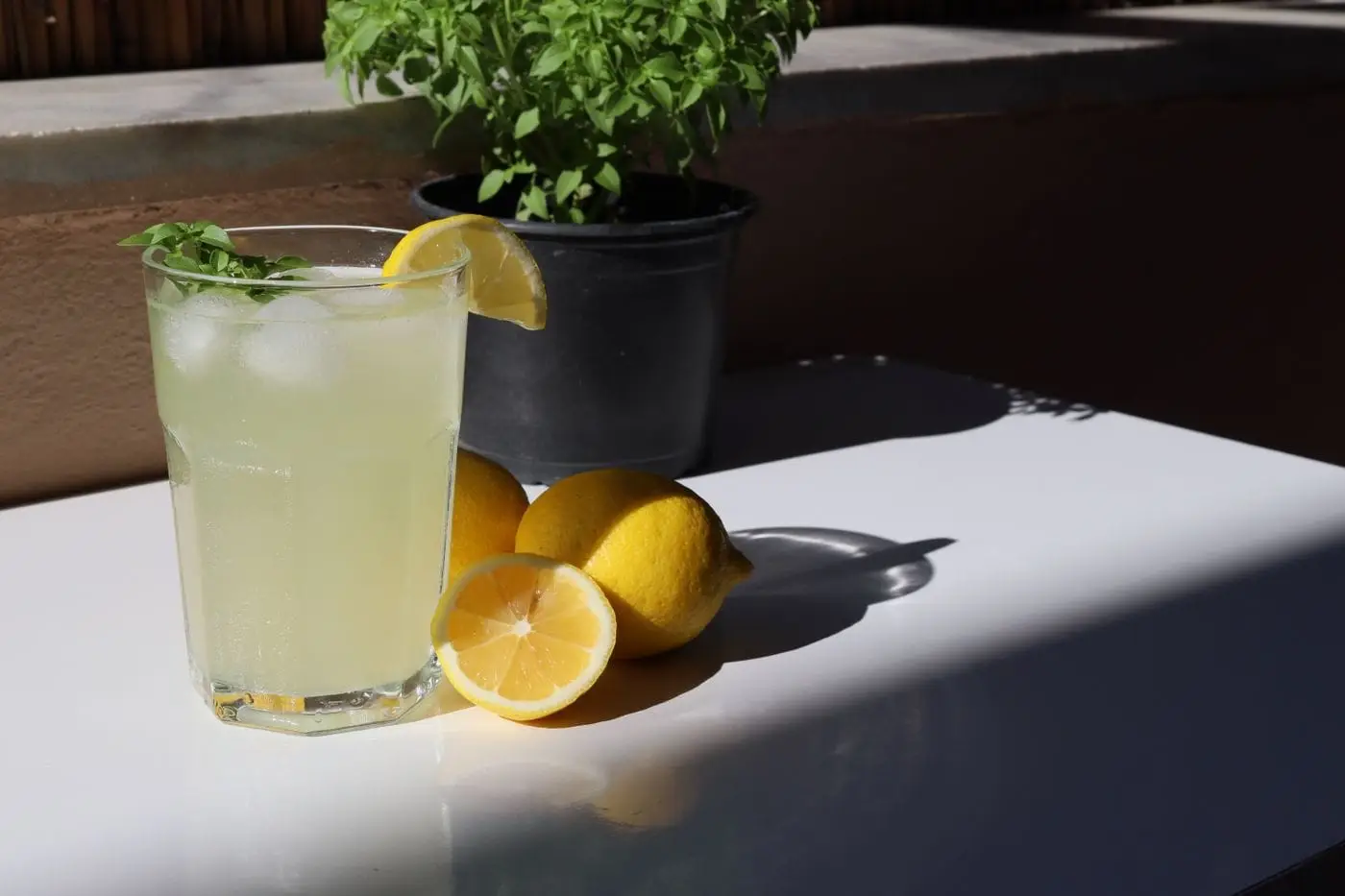 Glass of iced lemonade with lemon slice and basil beside fresh lemons