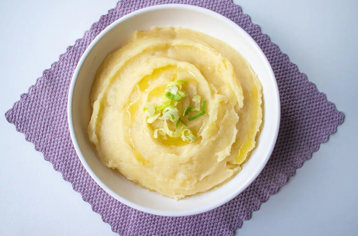 Bowl of creamy mashed potatoes topped with butter and sliced scallions