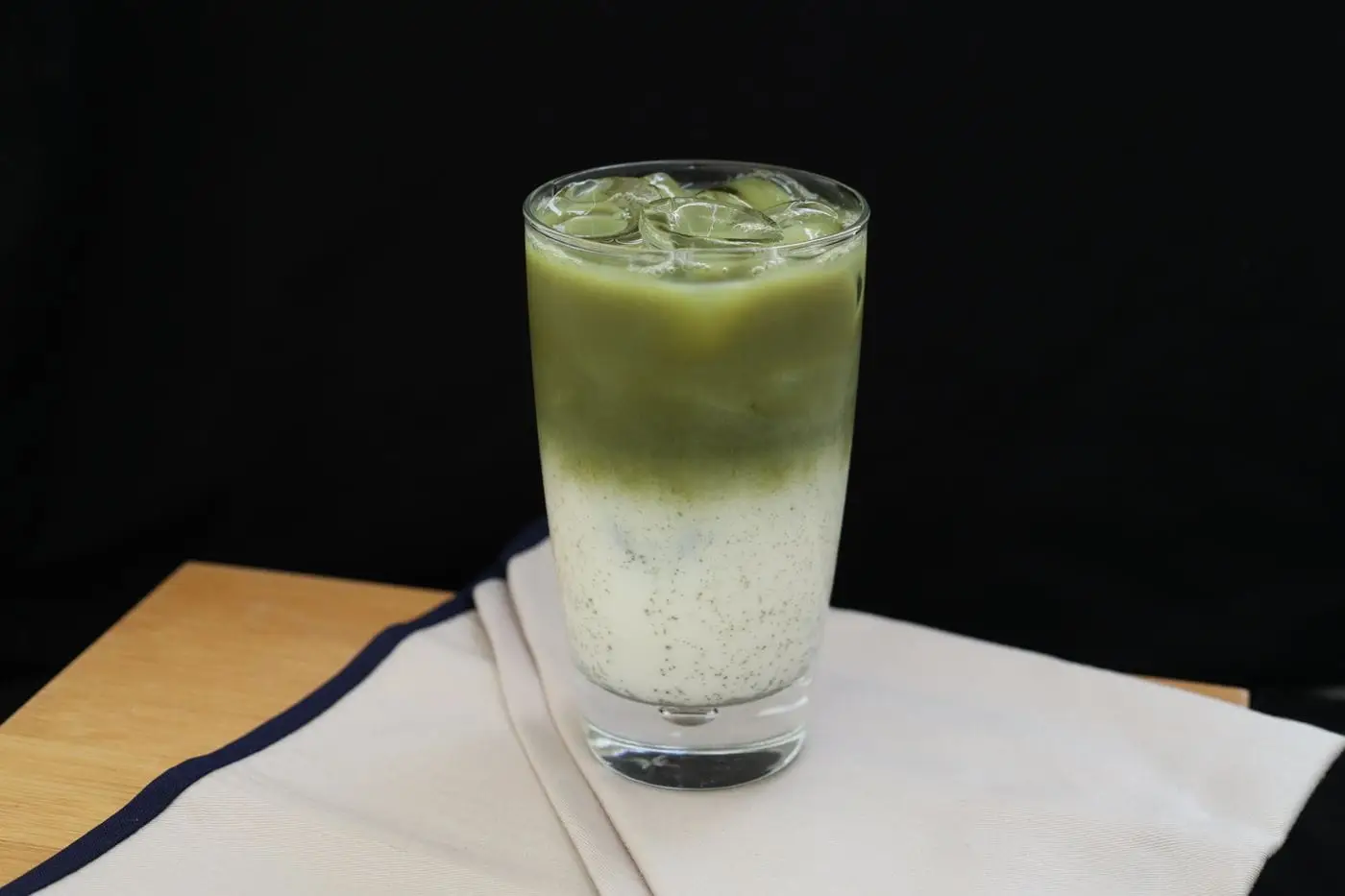 Iced matcha latte with green tea layered over milk in a tall glass