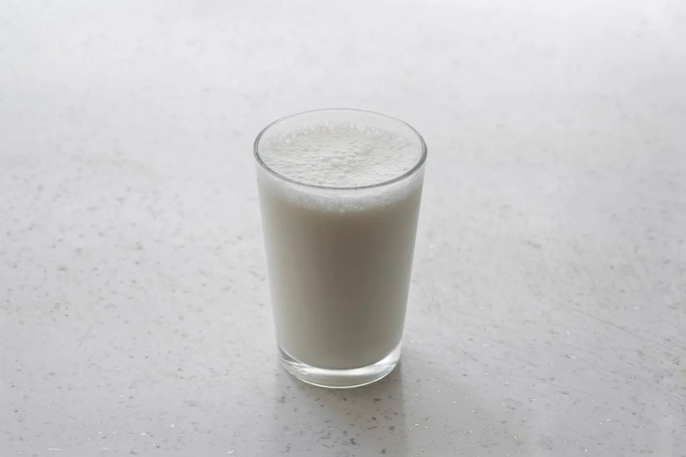 Glass of frothy fresh milk on a light speckled countertop
