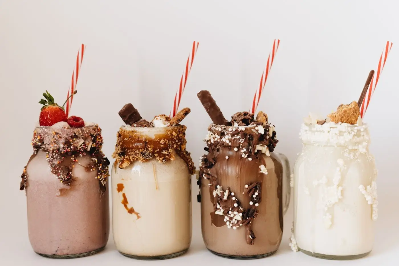 Four milkshakes in jars with candy toppings, drizzles and striped straws