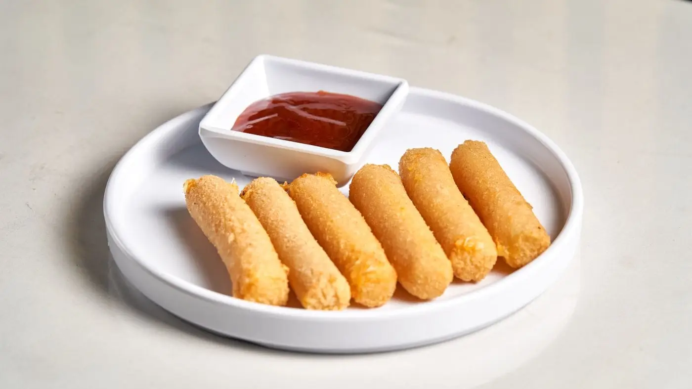Fried mozzarella sticks on a white plate with marinara dipping sauce