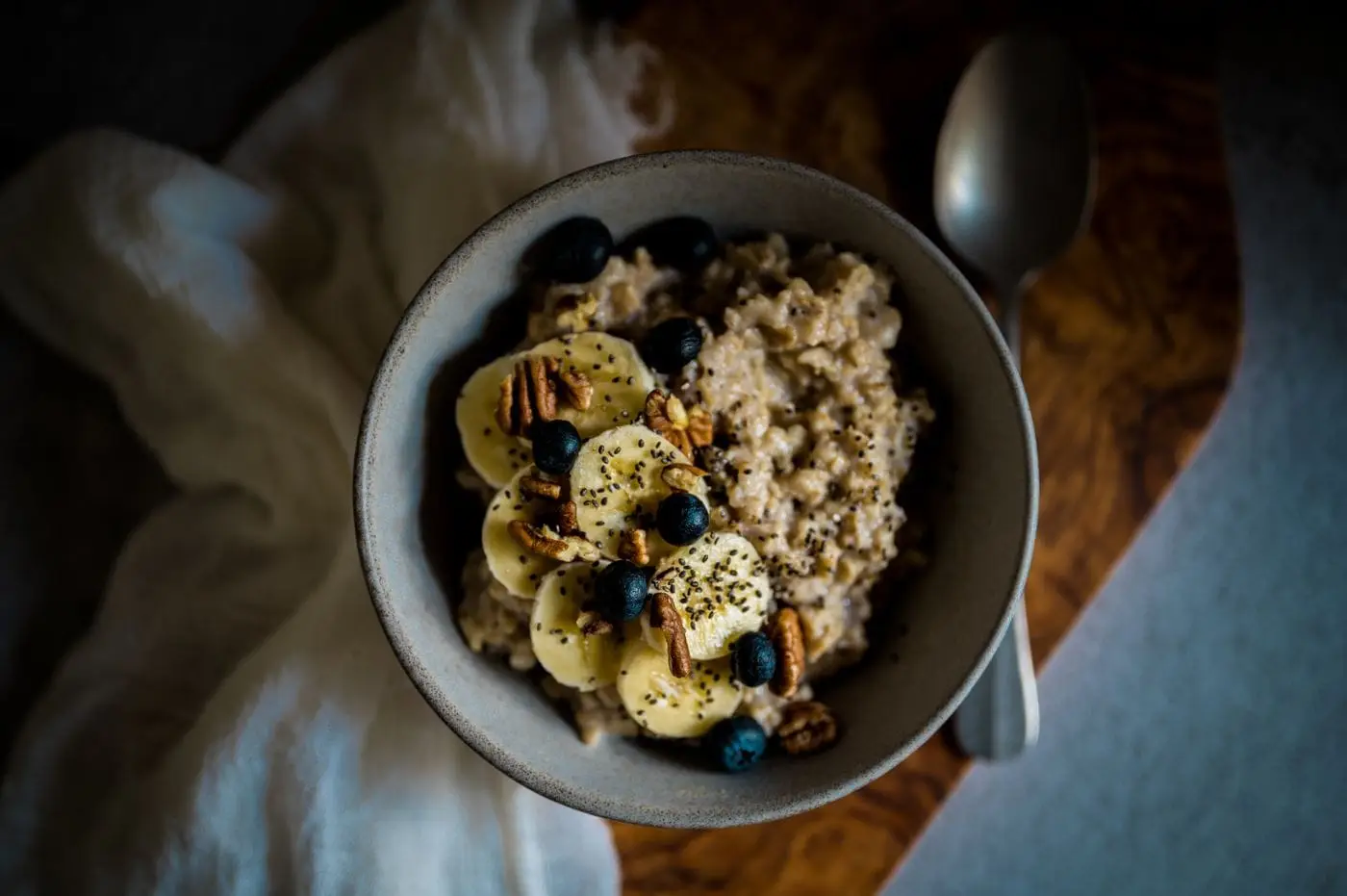 Bowl of oatmeal topped with banana slices, blueberries, pecans and chia seeds