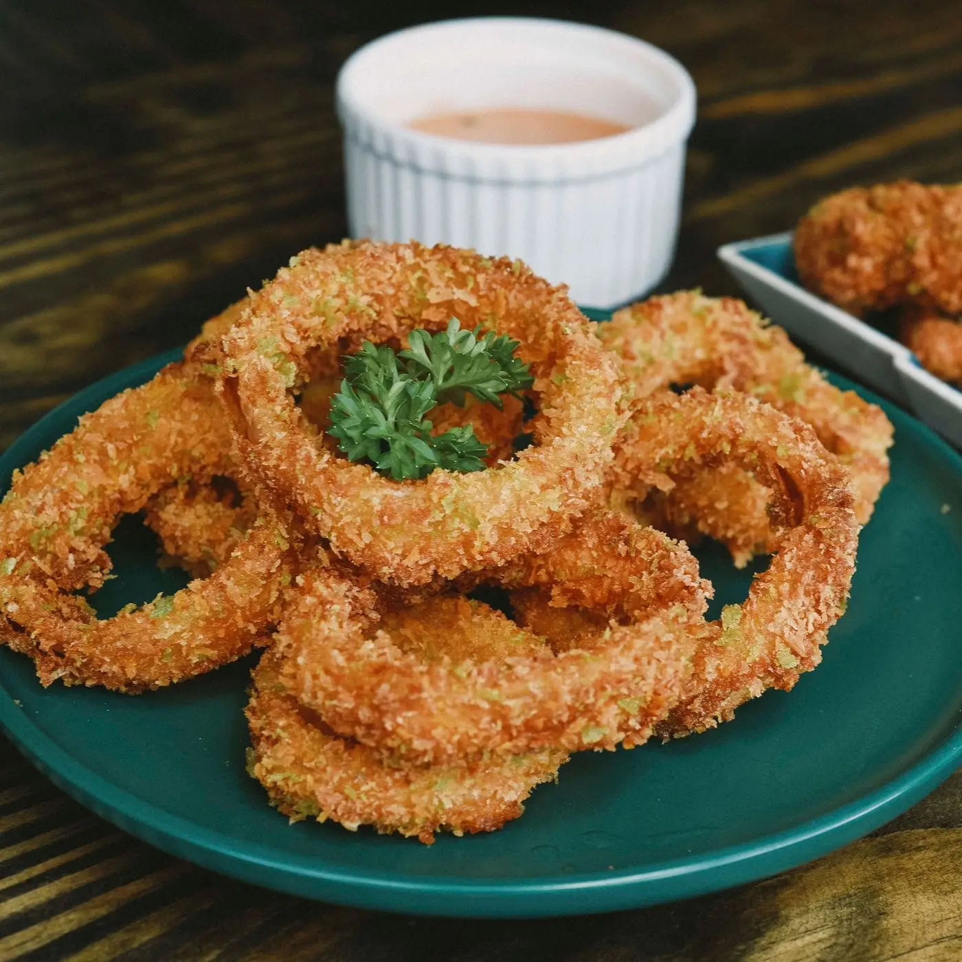 Crispy breaded onion rings on a green plate with dipping sauce