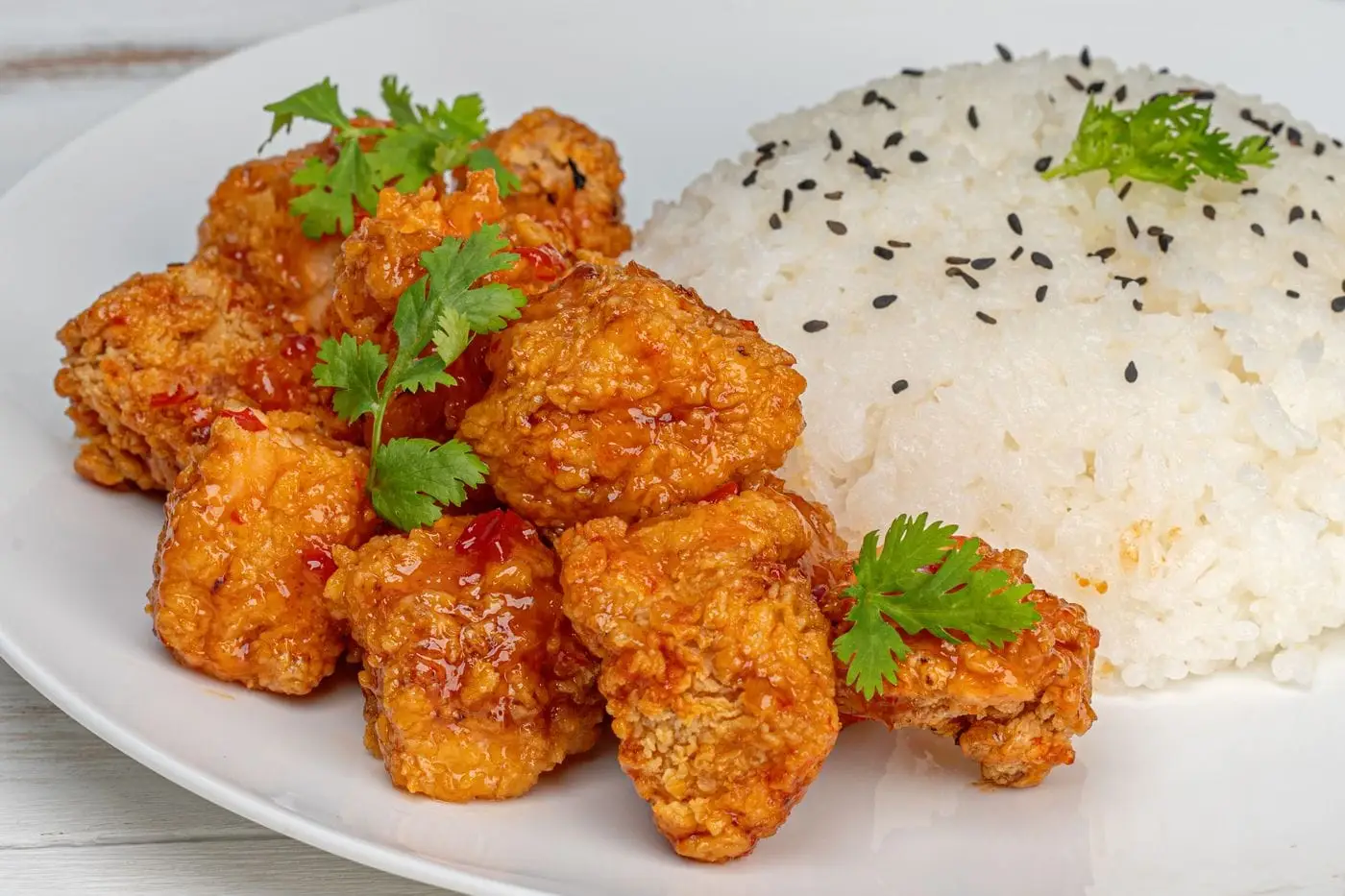 Crispy glazed fried chicken pieces with steamed white rice and sesame seeds