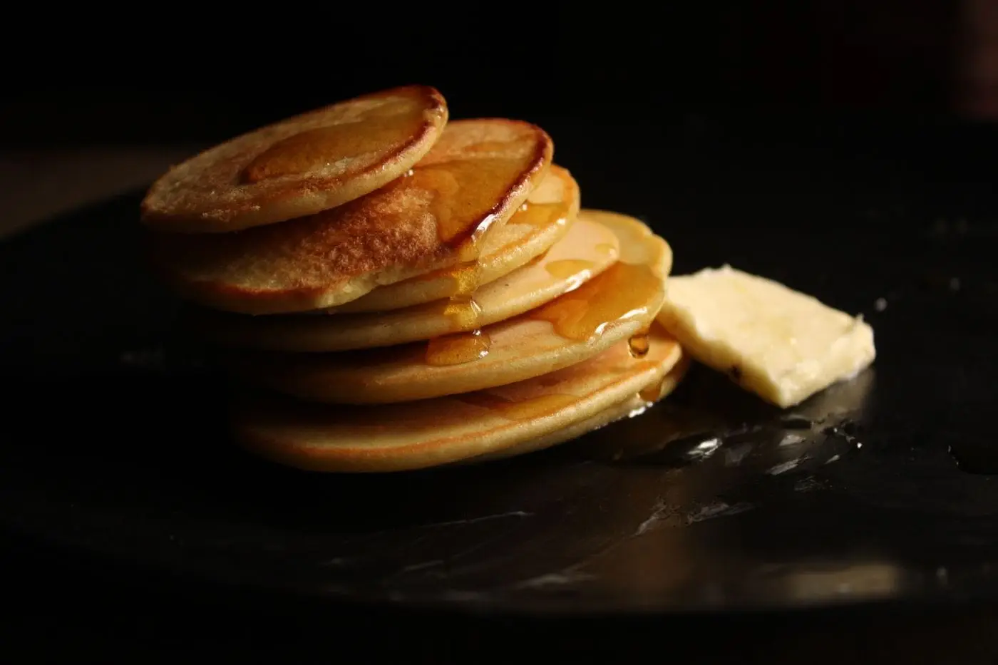 Stack of golden pancakes drizzled with syrup beside a pat of butter