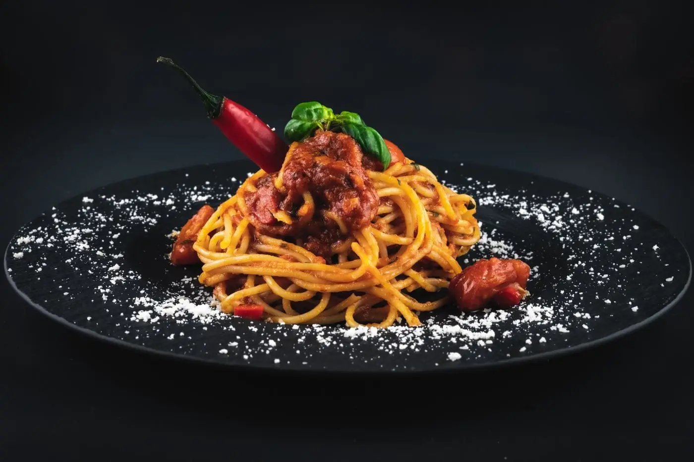 Spaghetti in tomato sauce with basil and grated cheese on a black plate